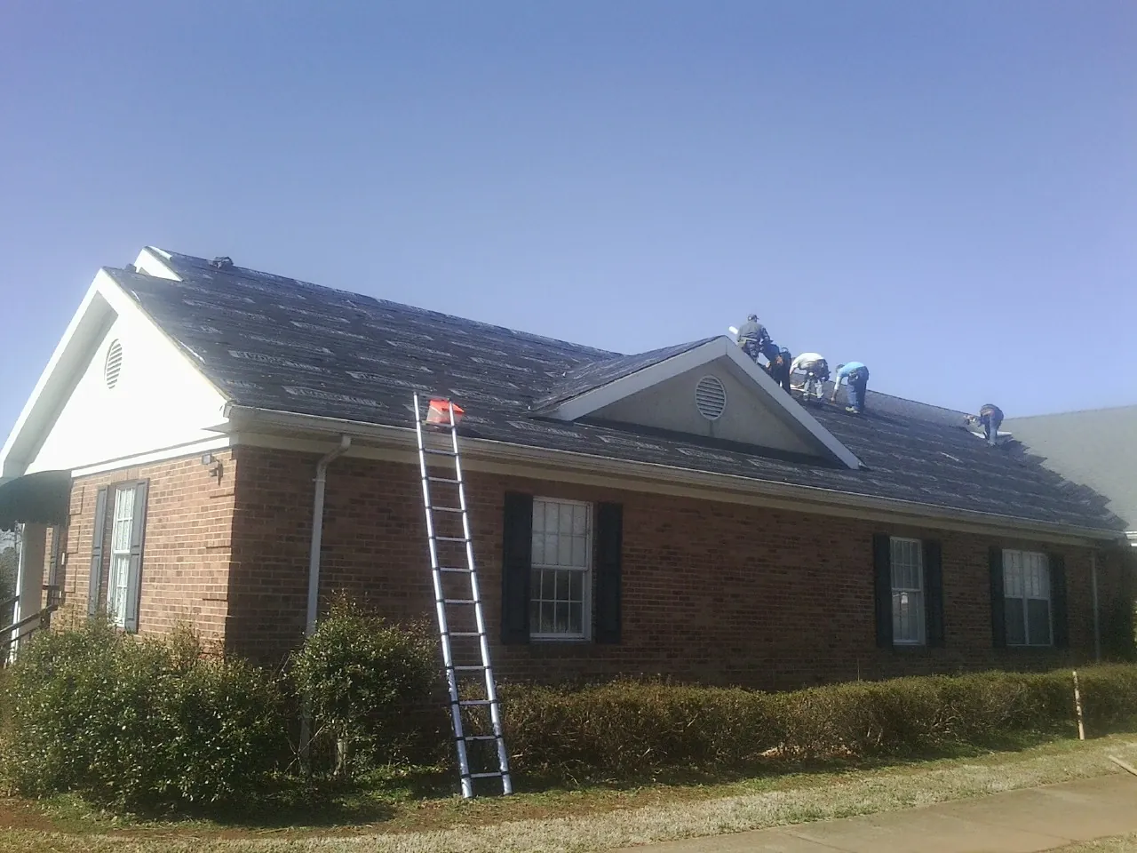 Crew tearing shingles off a brick ranch roof with a ladder set — Emergency Roof Repair work by our crew in High Falls