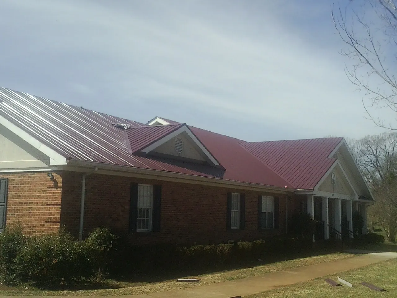 Red metal roof with gabled entries on a long brick building, from a Hail Damage Roof Repair job in High Falls