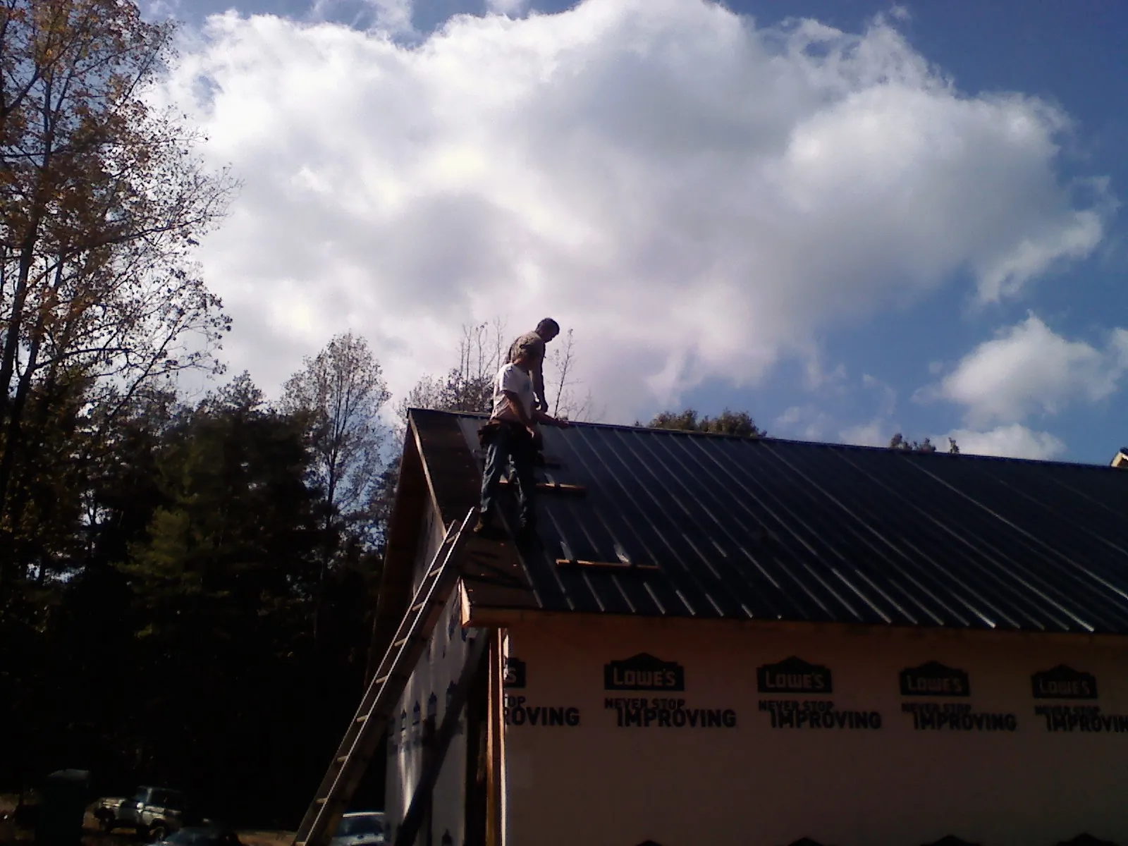 Roofer fastening dark metal panels high against a cloudy sky, from a Roof Inspection job in High Falls