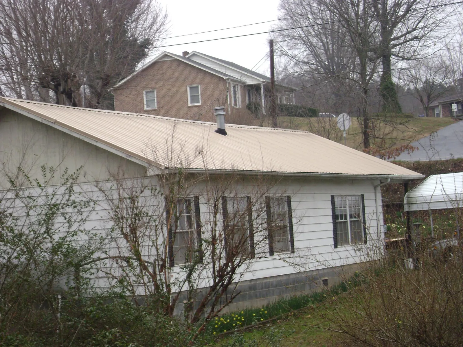 Tan metal roof on a white sided house set into a hillside — Commercial Roofing by Roofing Brothers in High Falls